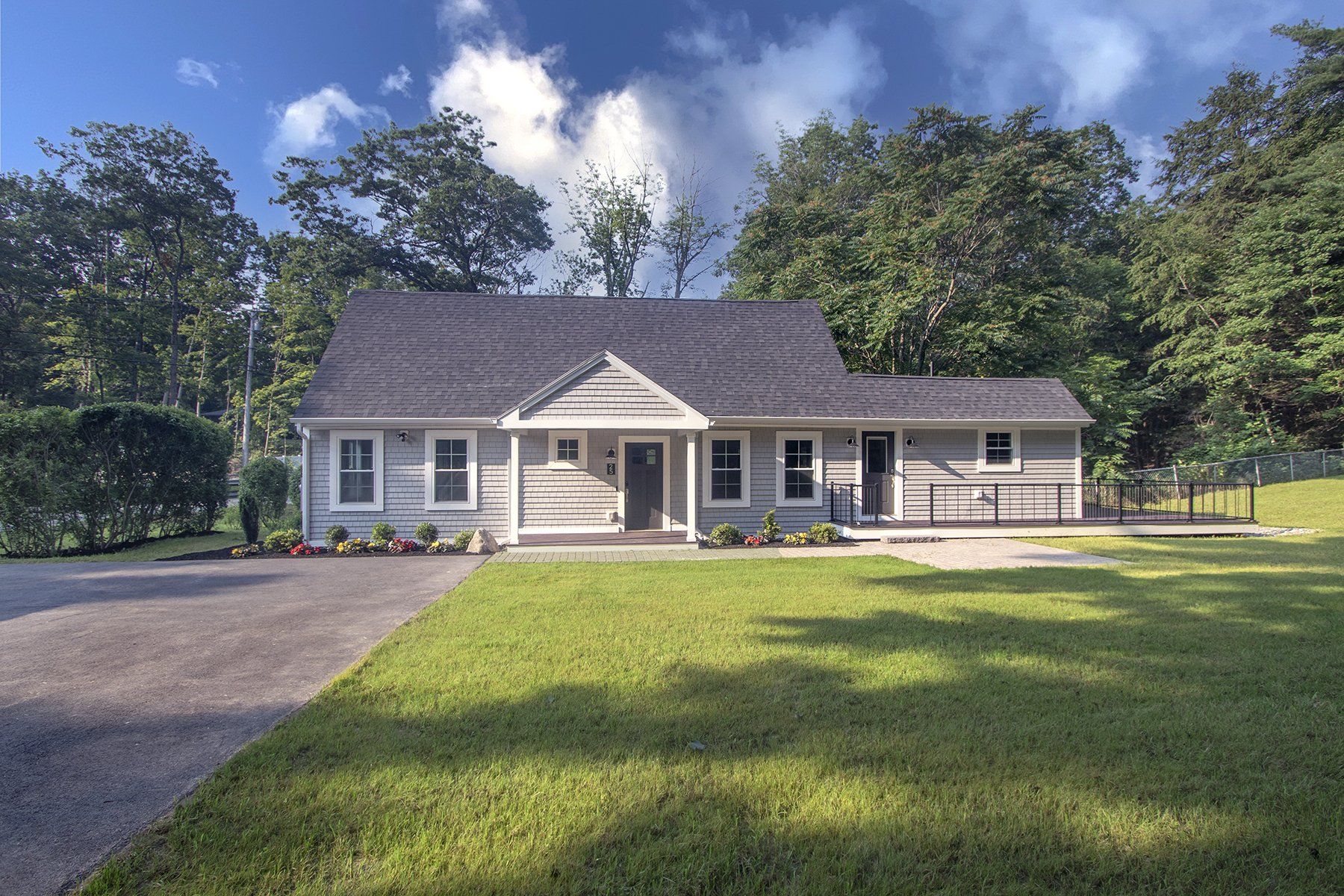 Exterior view of one story grey home large driveway and large front yard with green grass.