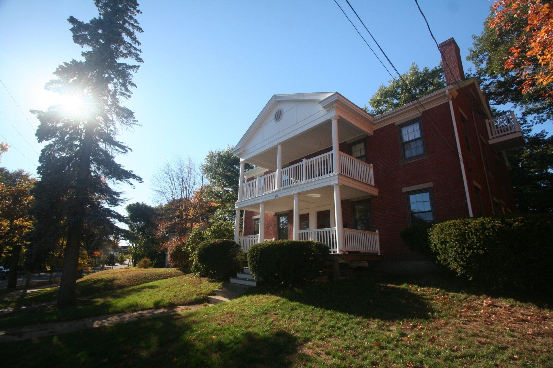 Exterior view of two story brick building  with a large balcony on each level, and large front yard with green grass and trees.