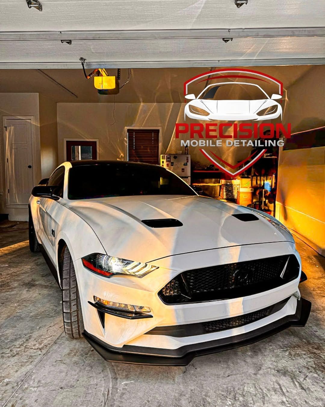 White sports car in a garage with a Precision Mobile Detailing sign in the background