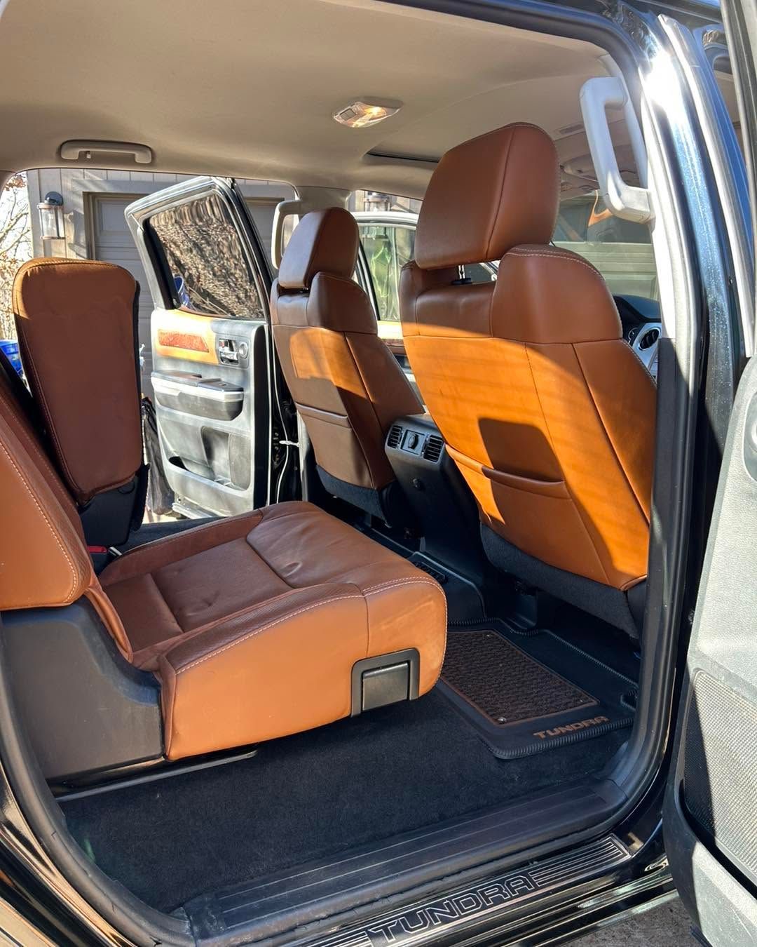 Open rear door showing tan leather car seats and interior, with sunlight on the back seat.