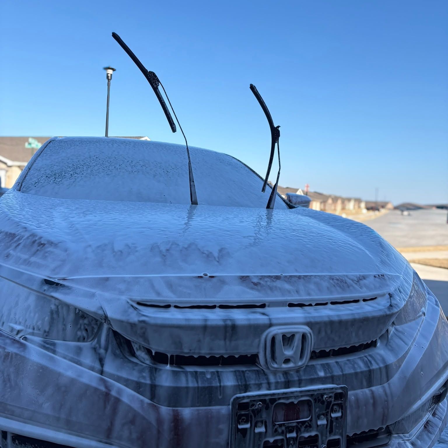 Snow-covered Honda parked outdoors with windshield wipers raised in a sunny lot