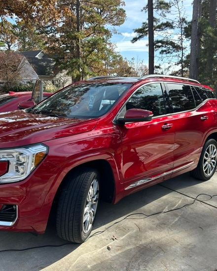 Red SUV parked in a driveway beside trees on a sunny day.