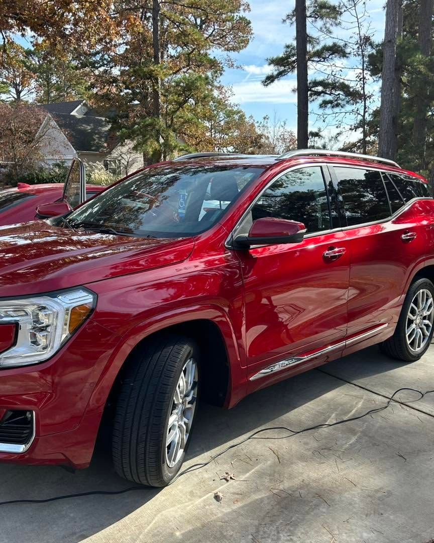 Red SUV parked in a driveway with trees and a house in the background.