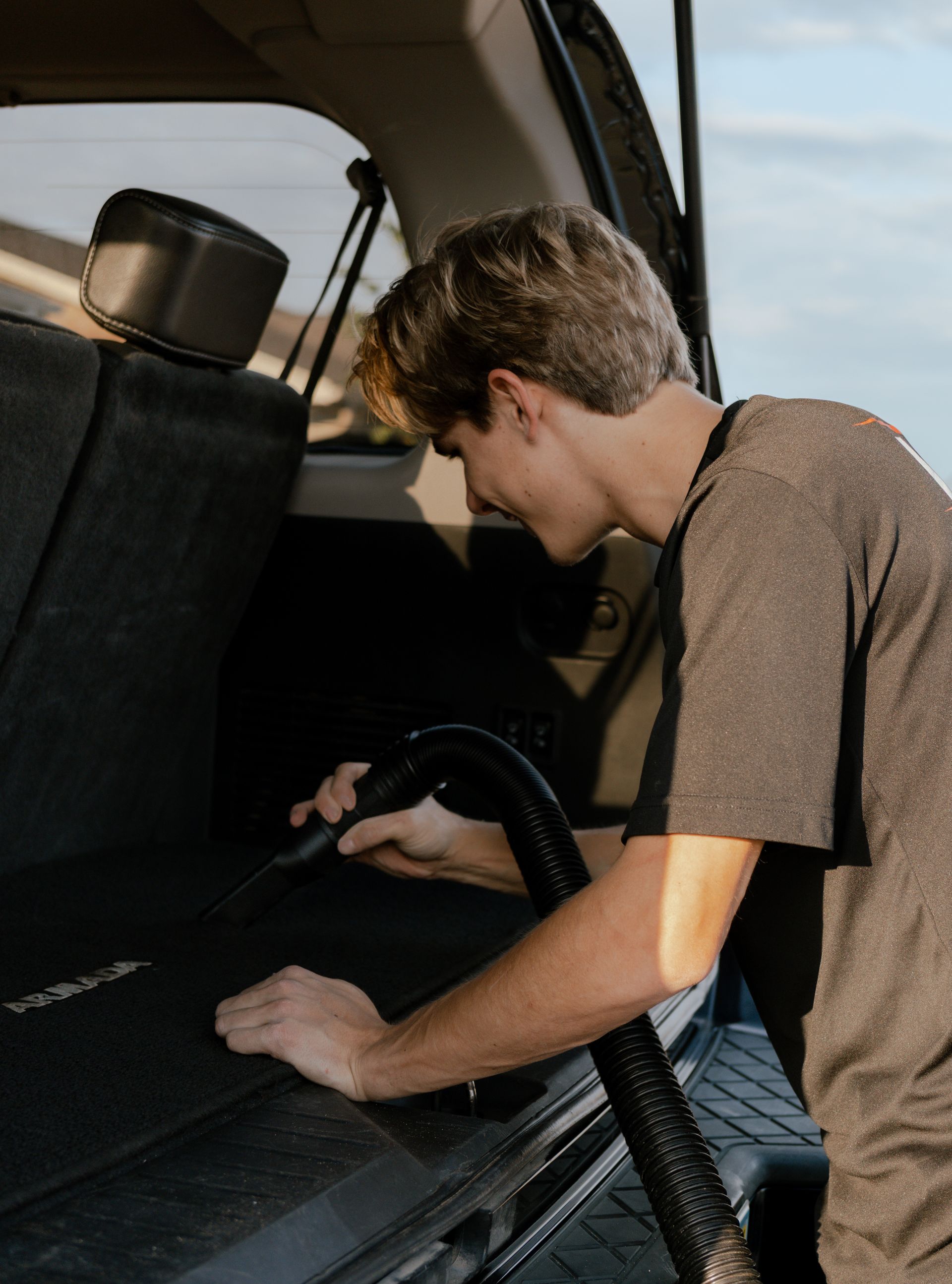 A person vacuuming the back seat of a car with a handheld hose