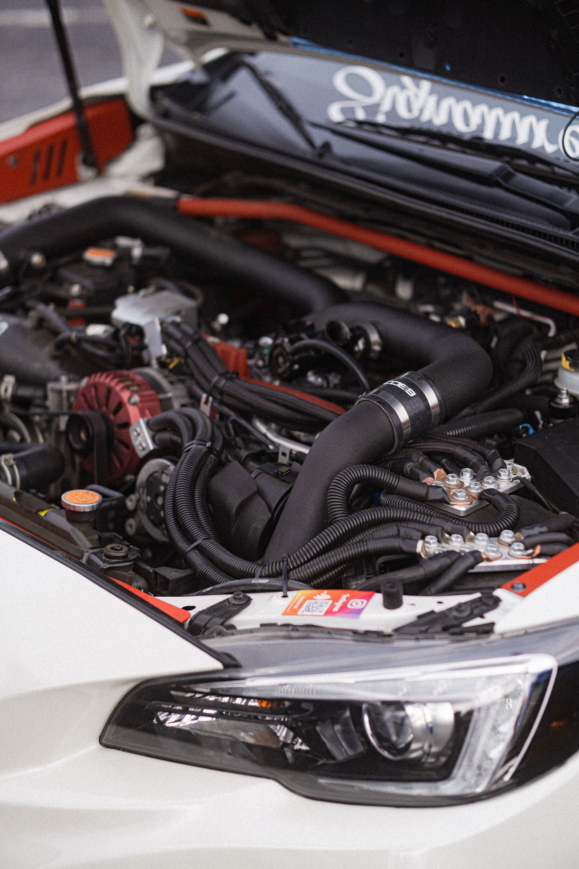 Car show display of a black car with hood open, revealing a modified engine bay and front headlight.