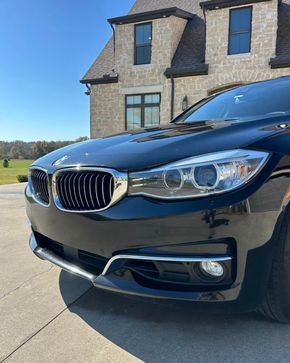 Black BMW sedan parked in front of a stone house on a sunny driveway