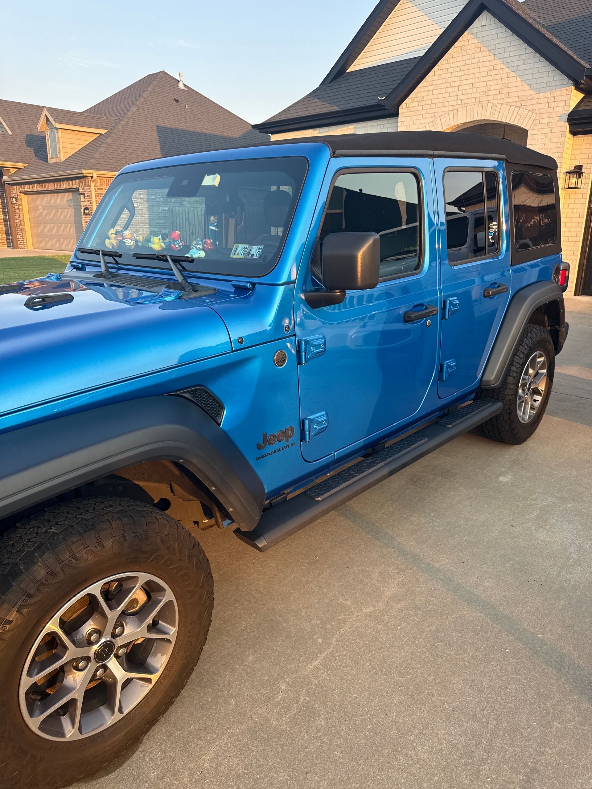 Blue Jeep Wrangler parked in a driveway beside a house at dusk