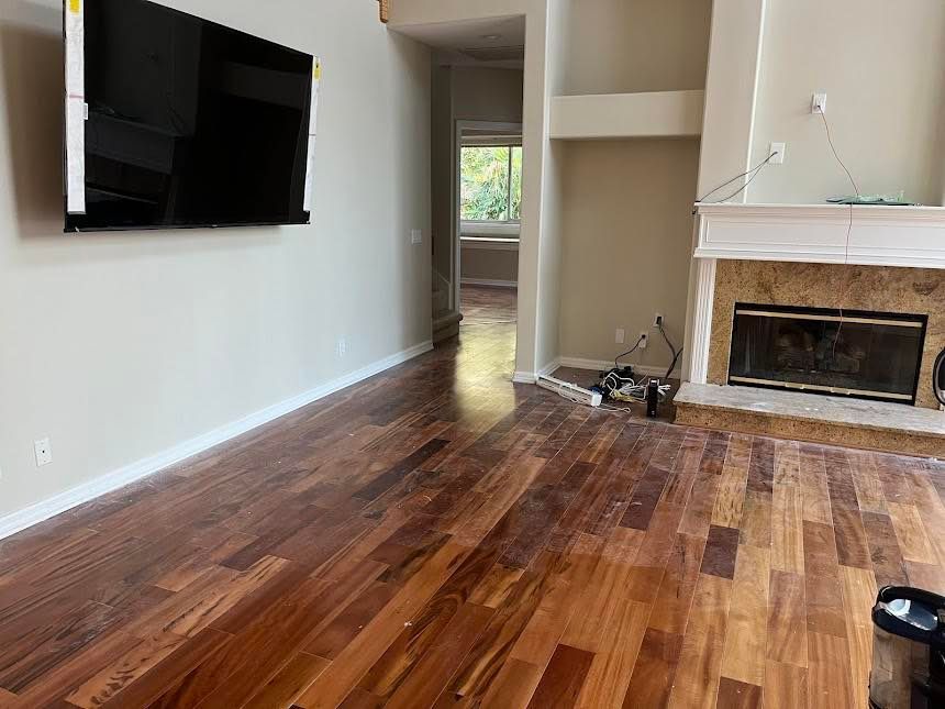 Newly installed hardwood floors in a living room with a fireplace, TV, and open doorway.