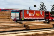 Lumber yard with stacked wood and a red delivery truck labeled “The Best in Lumber”