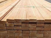 Stacked wooden planks on a construction site, viewed from the end with visible wood grain.