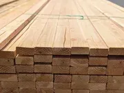 Stacked wooden planks on a construction site, viewed from the end with visible wood grain.