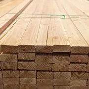 Stacked wooden planks on a construction site, viewed from the end with visible wood grain.