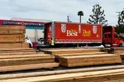 Lumber yard with stacked wood and a red delivery truck labeled “The Best in Lumber”