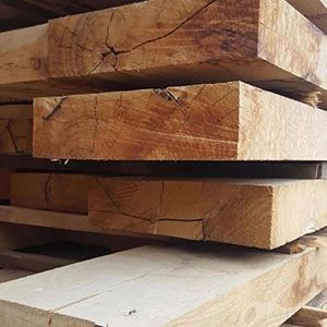 Stacked rough-cut wooden planks on a pallet, shown close-up with visible grain and cracks.