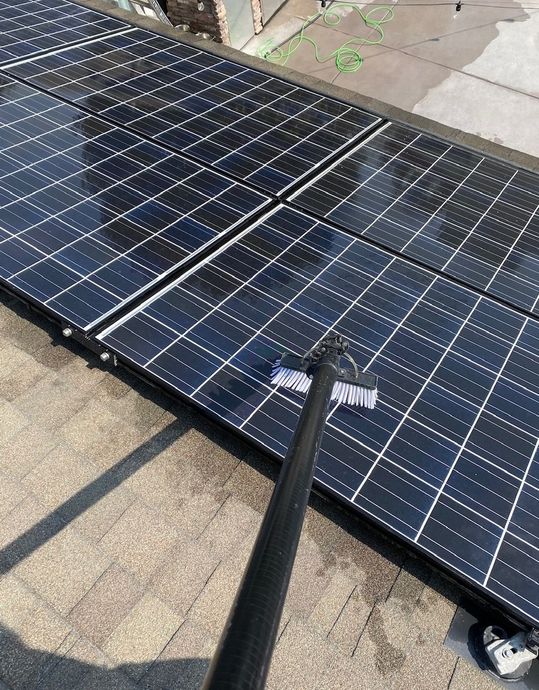 A person pressure-washing two large solar panels on a rooftop.