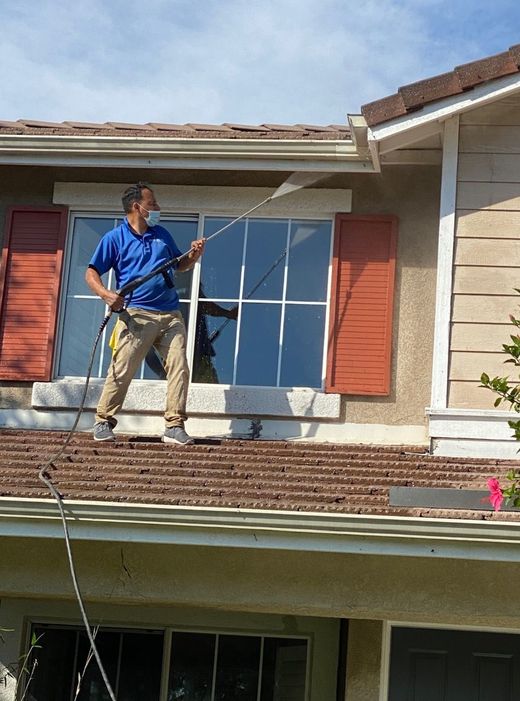 Worker spraying a house roof from the upper floor with a long pole
