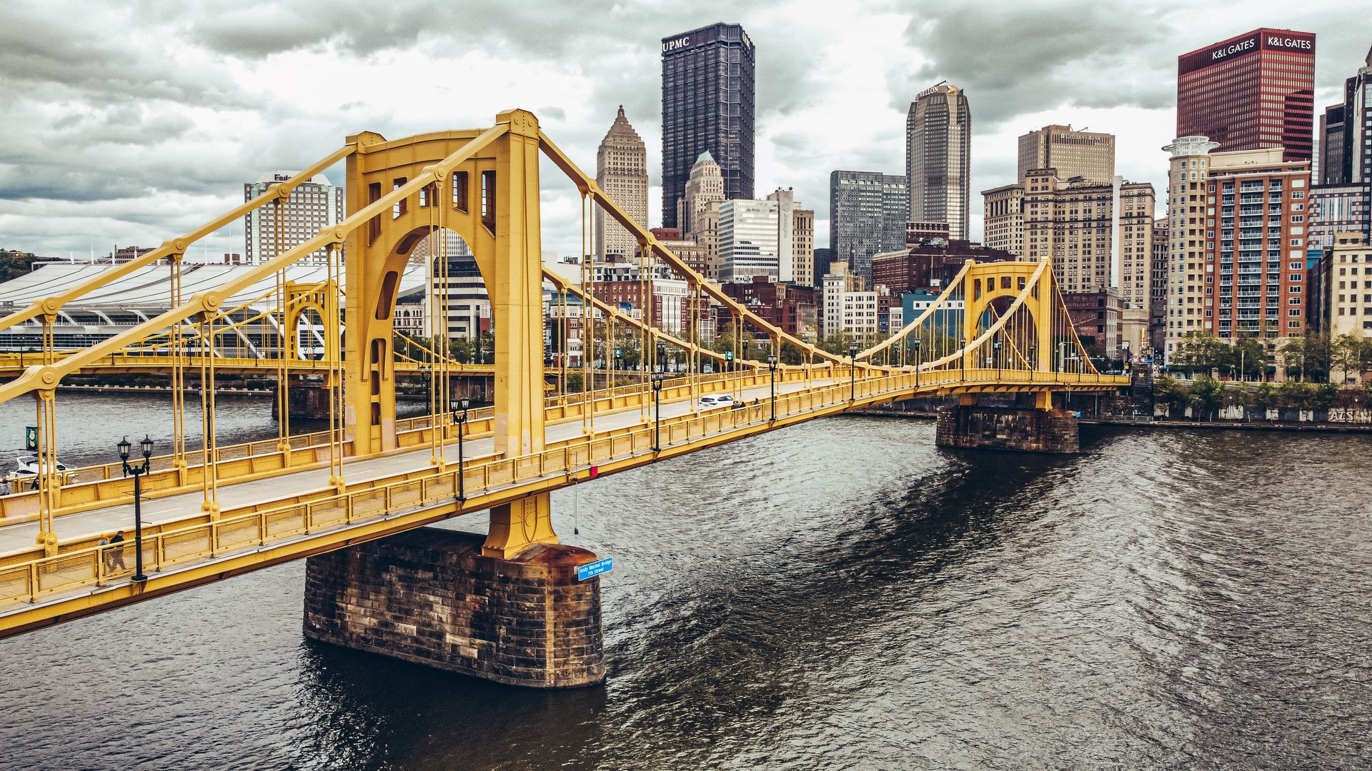 A yellow bridge over a river with a city skyline in the background.