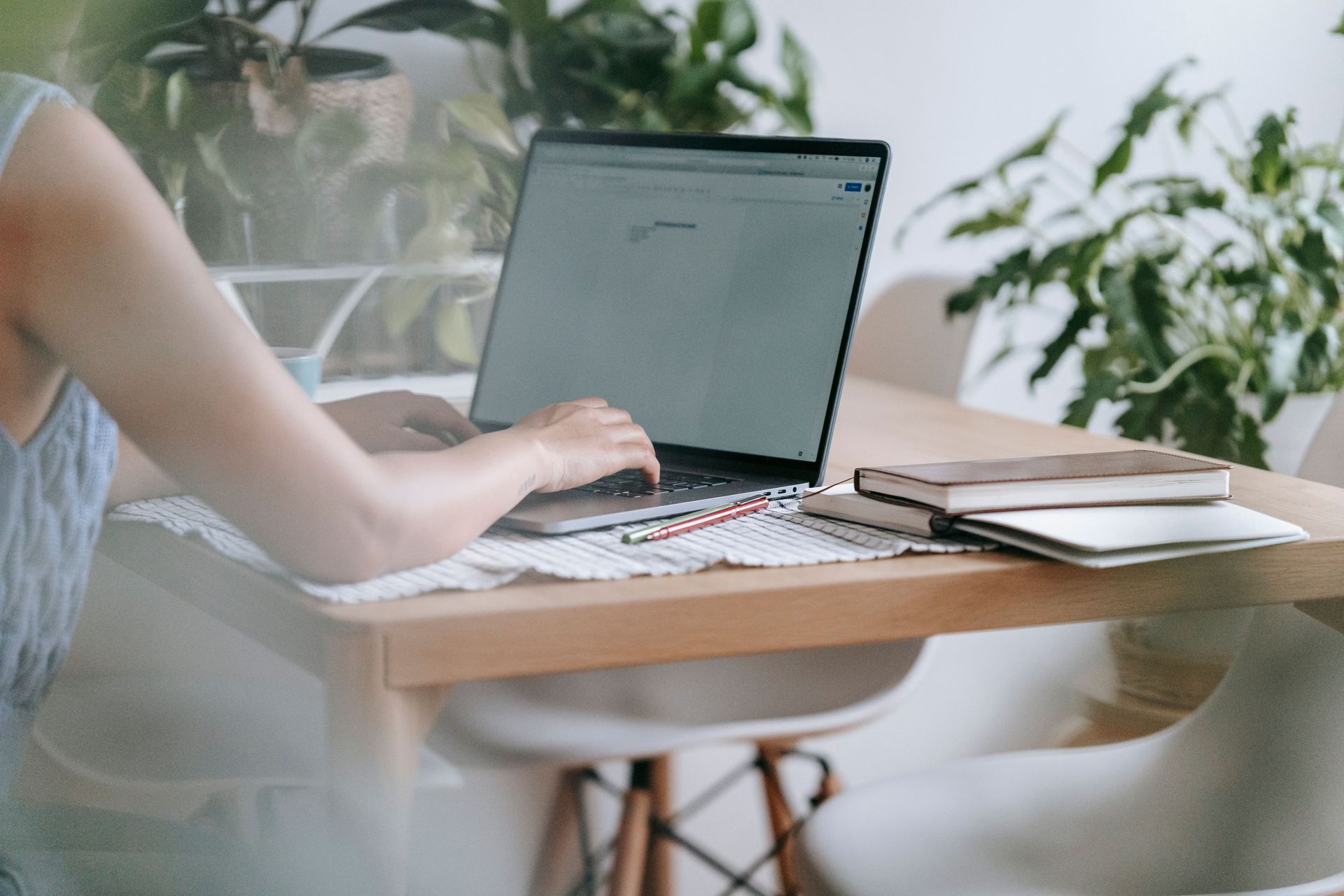 Person using a laptop at a wooden desk with plants in a bright home office