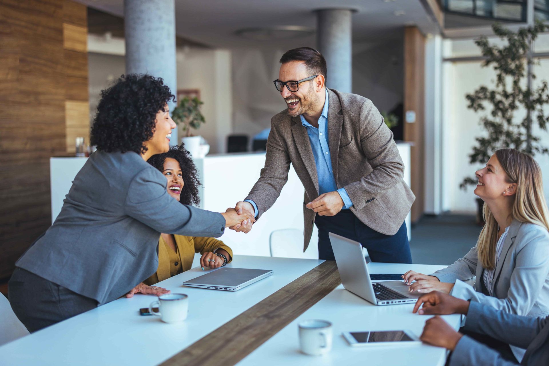 Three coworkers shaking hands in a modern office during a meeting