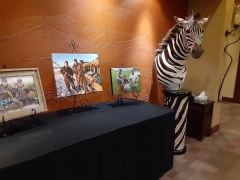 A zebra statue is sitting on top of a table next to paintings.
