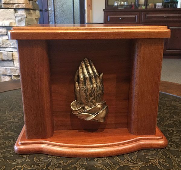 A wooden urn with a statue of praying hands on top of it.