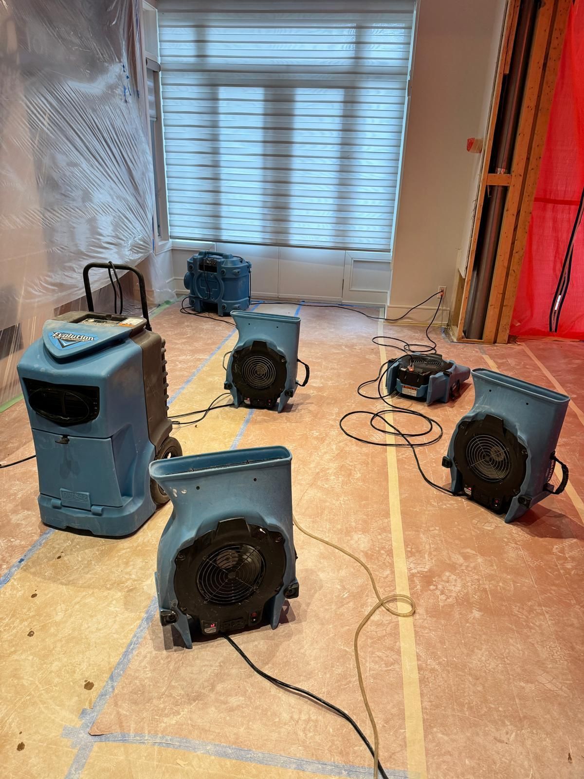 Five black portable speakers and cables scattered on a bare floor in a room under renovation.