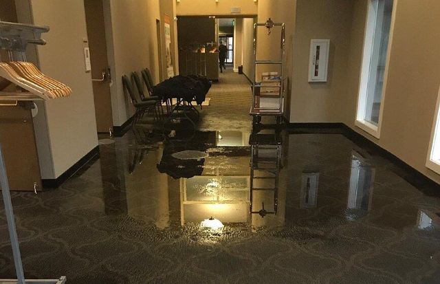 Flooded hallway with standing water reflecting lights and chairs along the walls