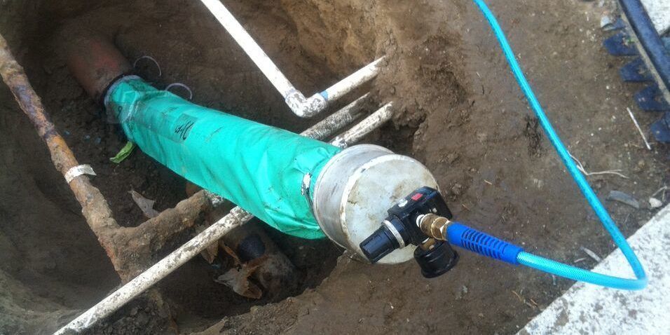 Green-wrapped pipe joint in a trench, with blue hose and white clamps attached