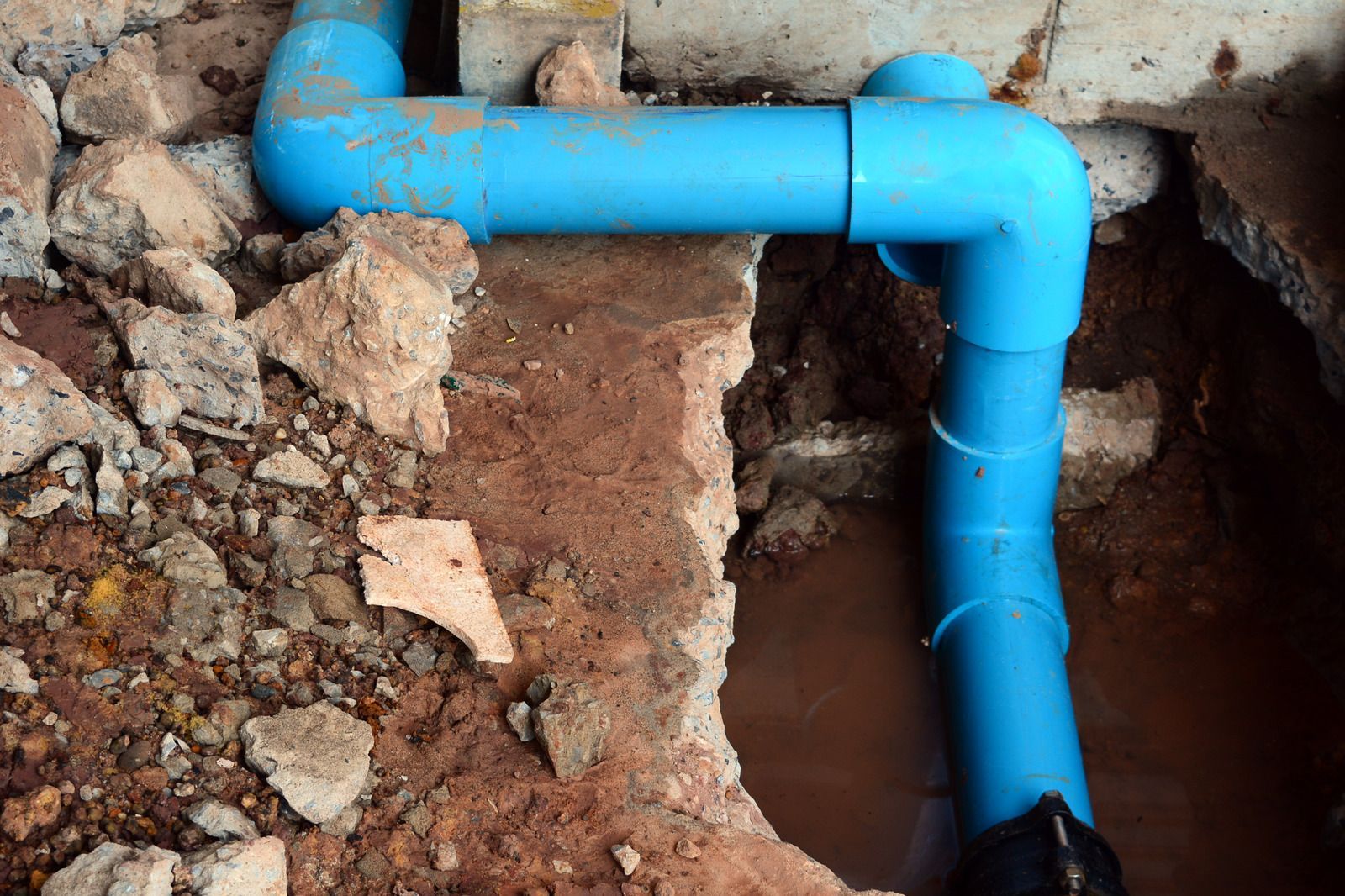 Blue PVC pipe running through a rough dirt trench and into a wall opening