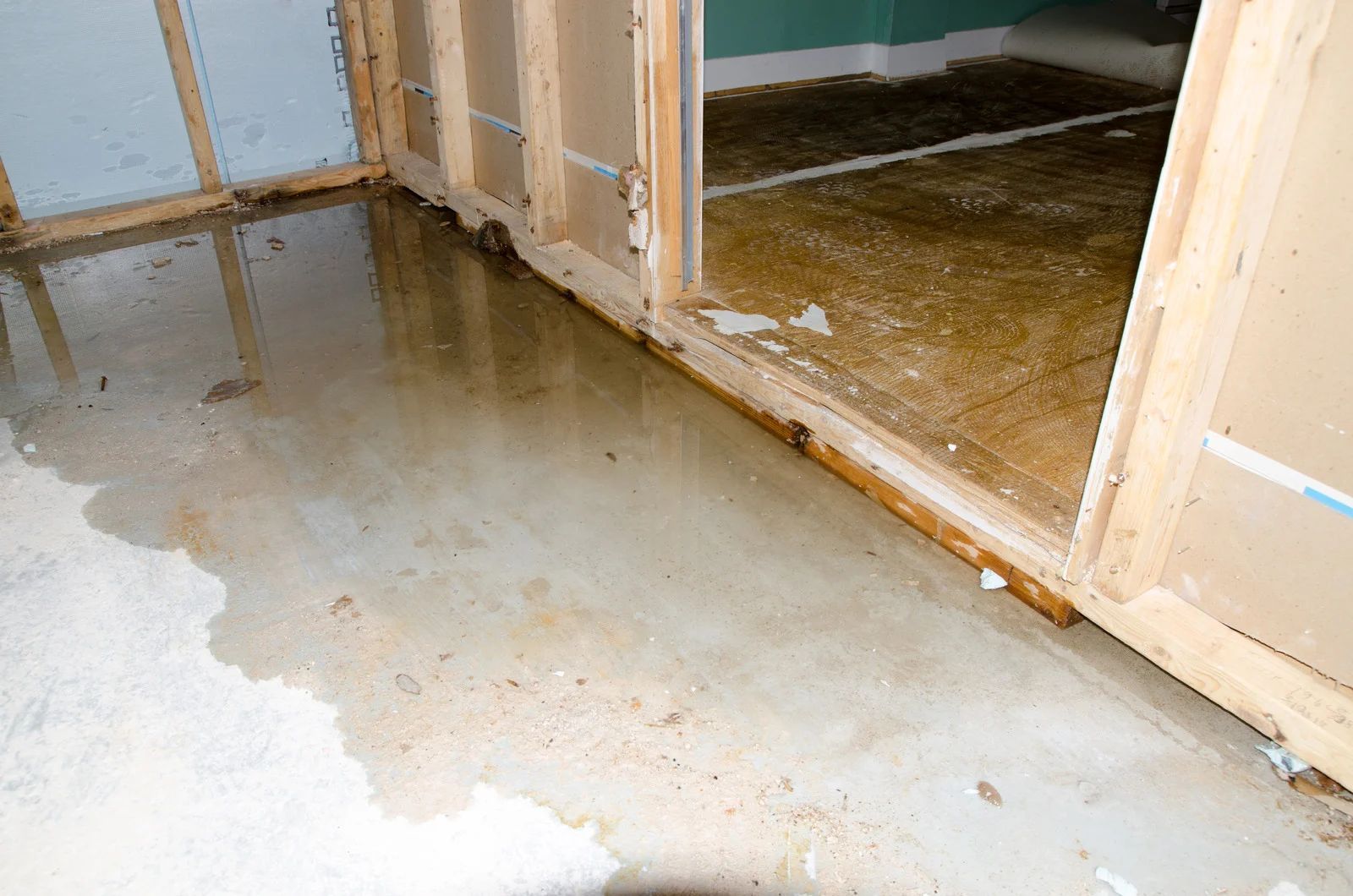 Water-damaged floor beside open wall studs and doorway framing in an unfinished room