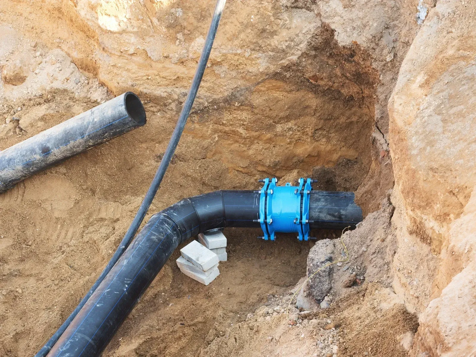 Black plastic pipe in a dirt trench, connected with a blue clamp fitting