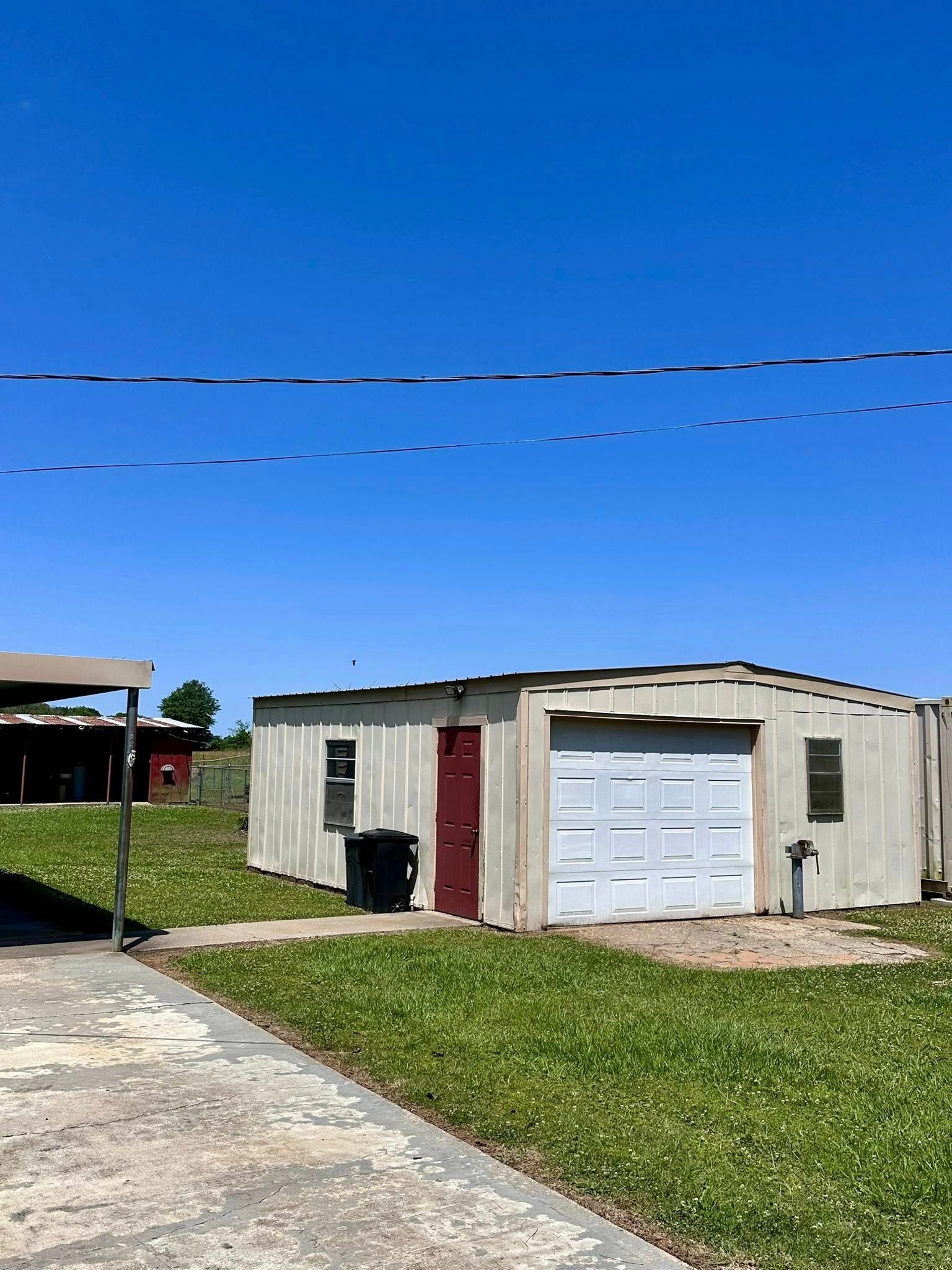 Small white garage with a red door and white garage door beside a concrete driveway under a blue sky.