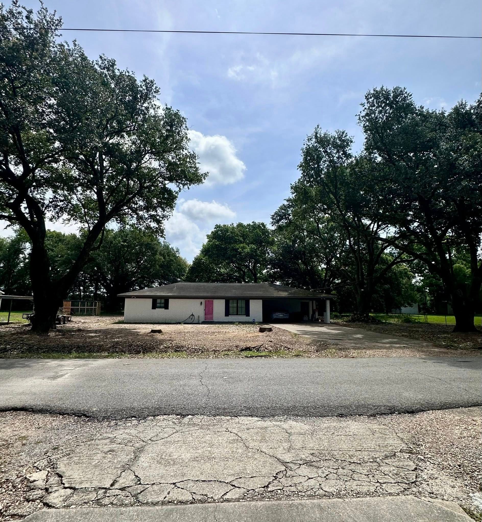 Single-story house with trees, a gravel driveway, and cloudy sky above.