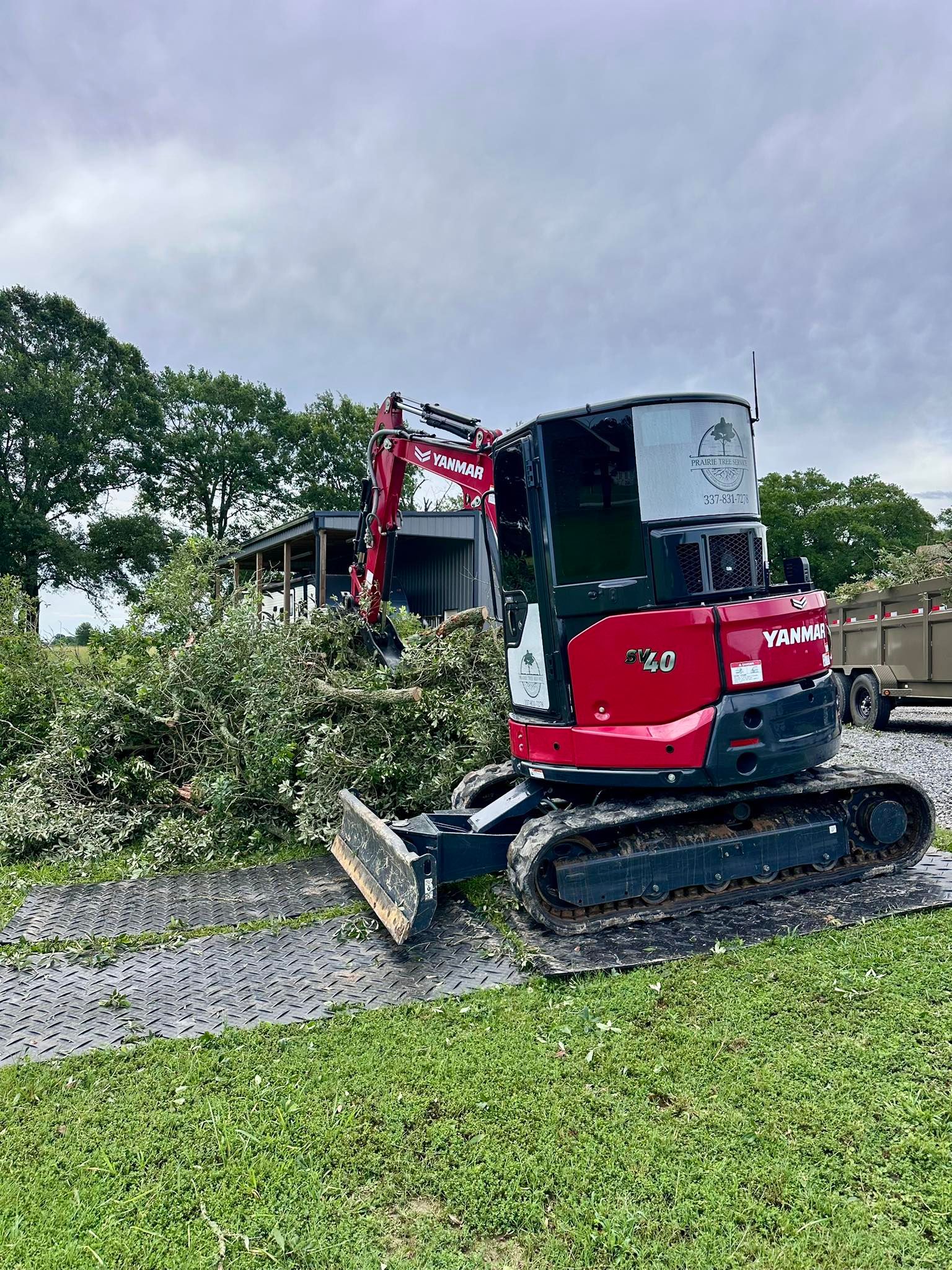 Red excavator clearing gravel near a grassy roadside under cloudy skies