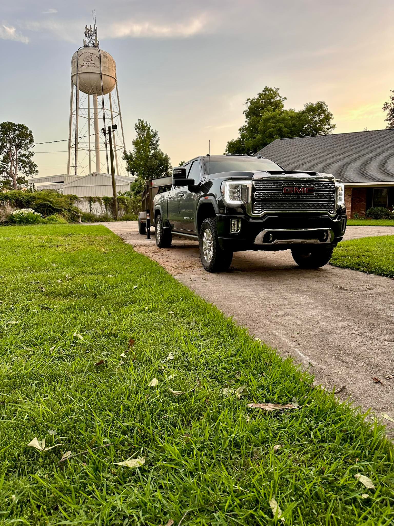 Black pickup truck parked on a driveway beside a green lawn, with a water tower in the background.