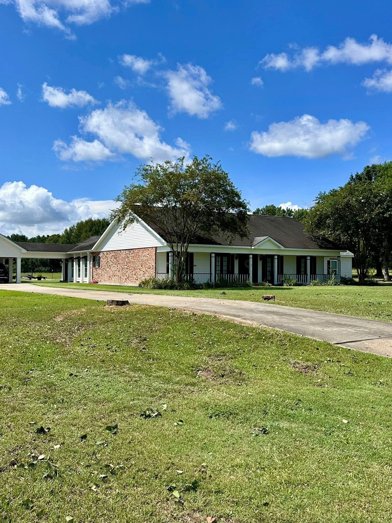 Single-story house with white porch and brick gable, set on a grassy lawn under a blue sky with clouds.