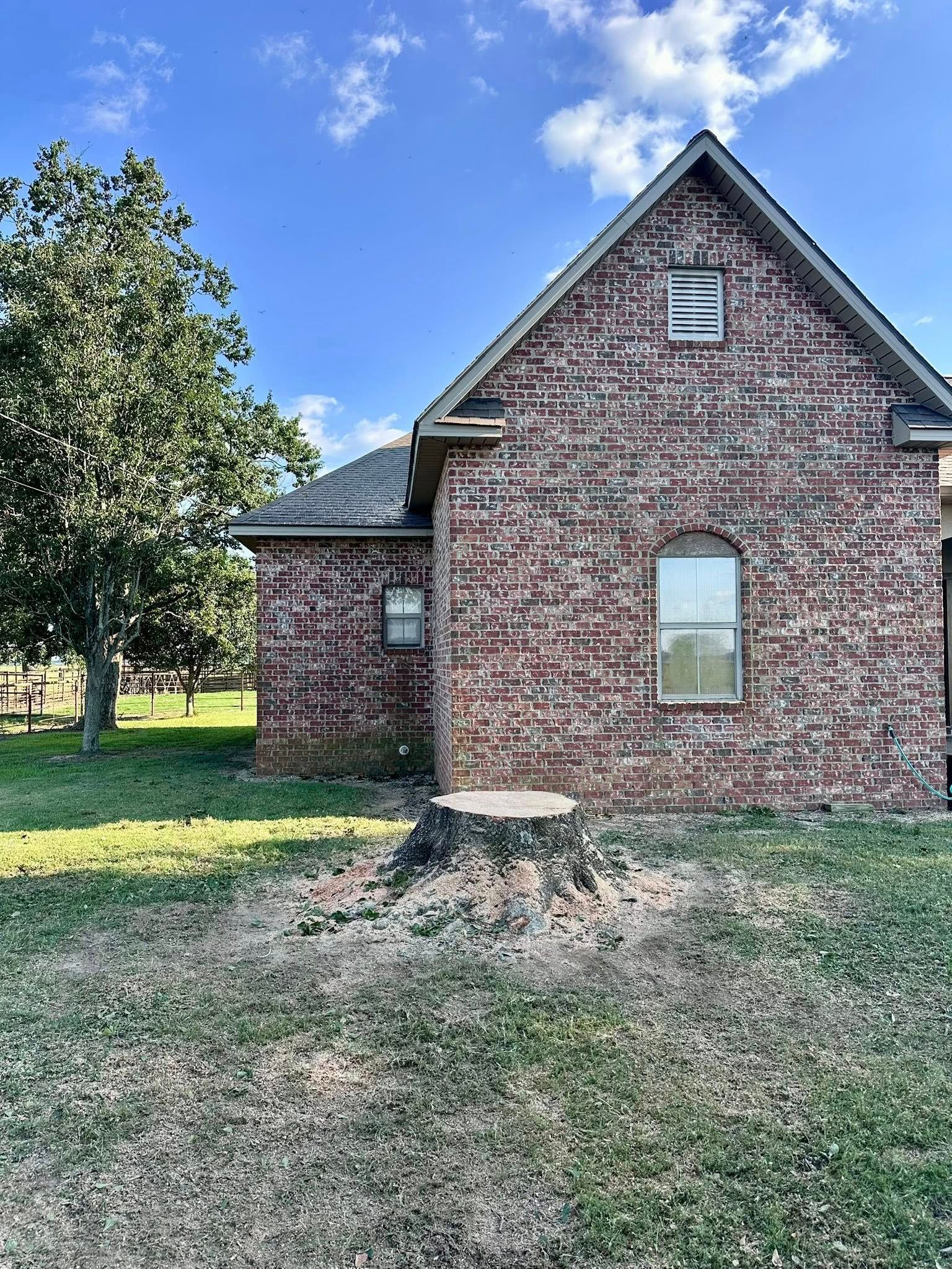 Brick house exterior with gabled roof, small windows, and grassy yard under a blue sky