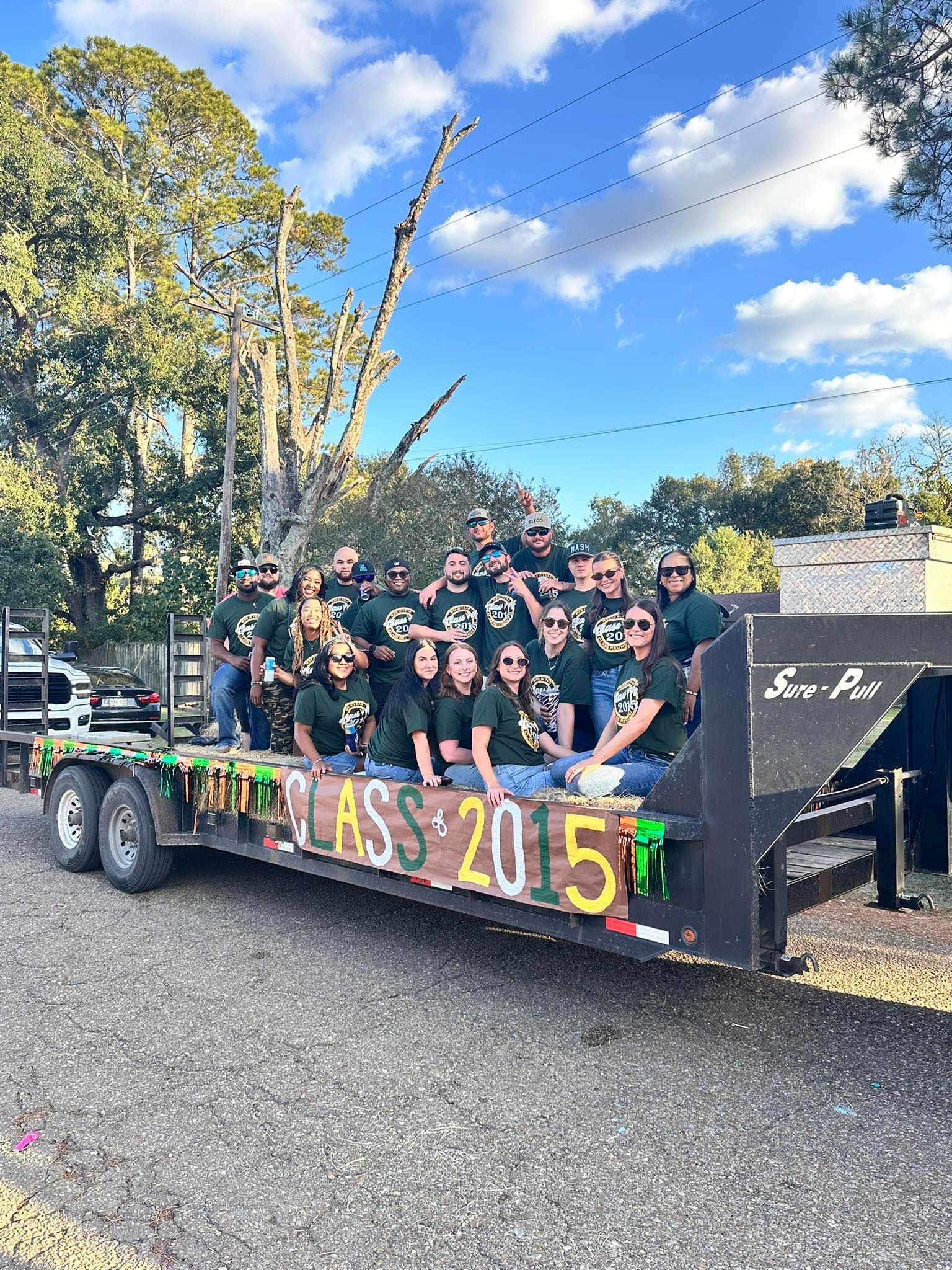 Group of people in black shirts posing on a decorated parade float outdoors under a blue sky.