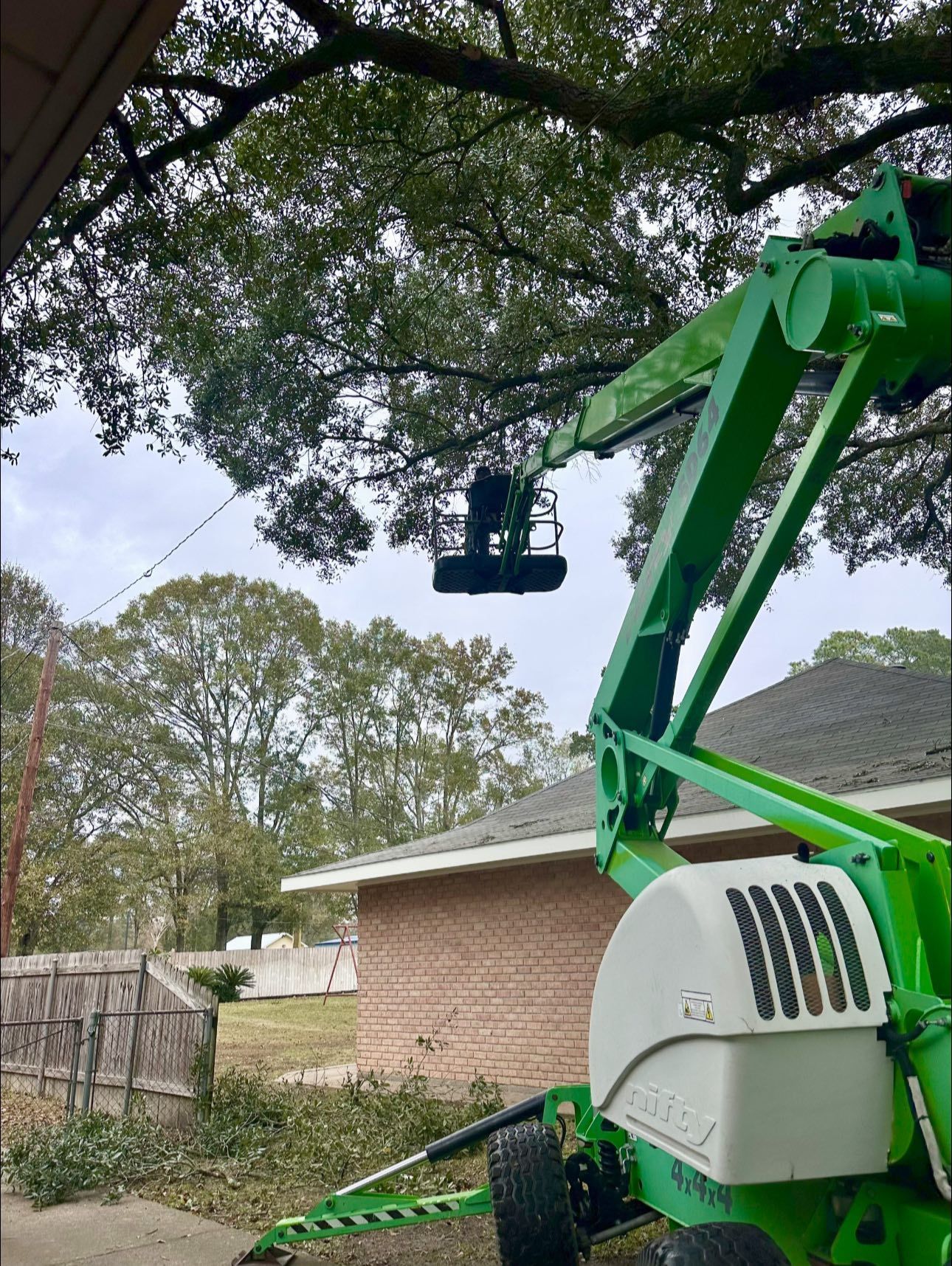 Green boom lift extended over a yard beside a brick house and trees