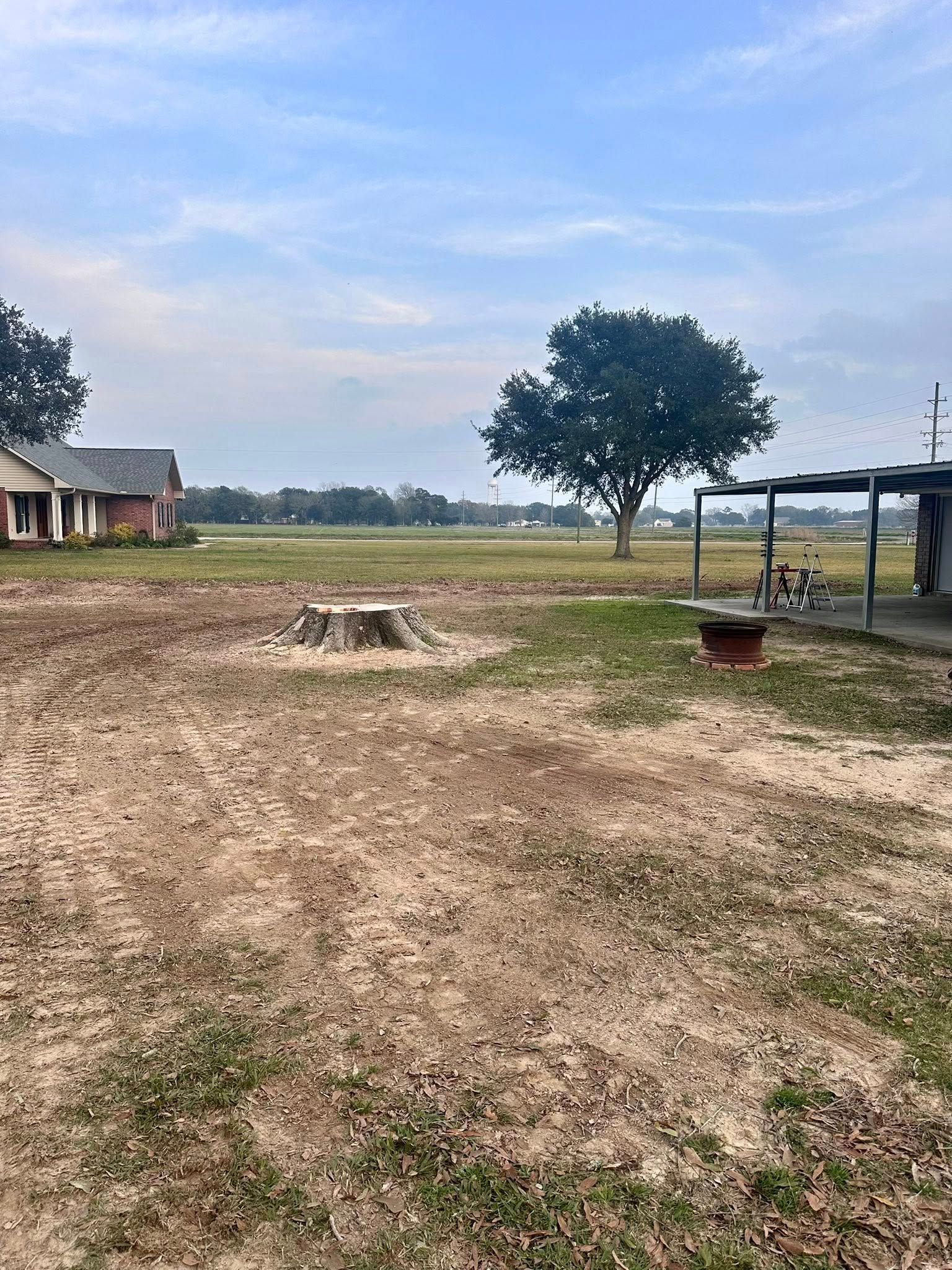 Open dirt yard with a tree, small buildings, and a shelter under a cloudy sky
