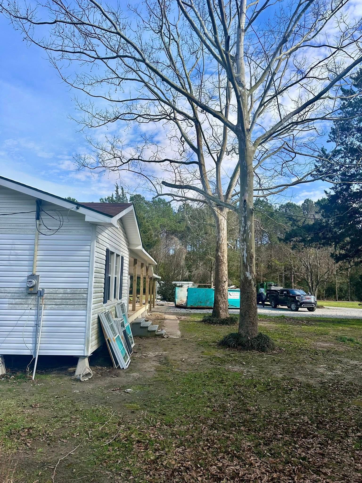 White house exterior beside a yard with a leafless tree and blue sky