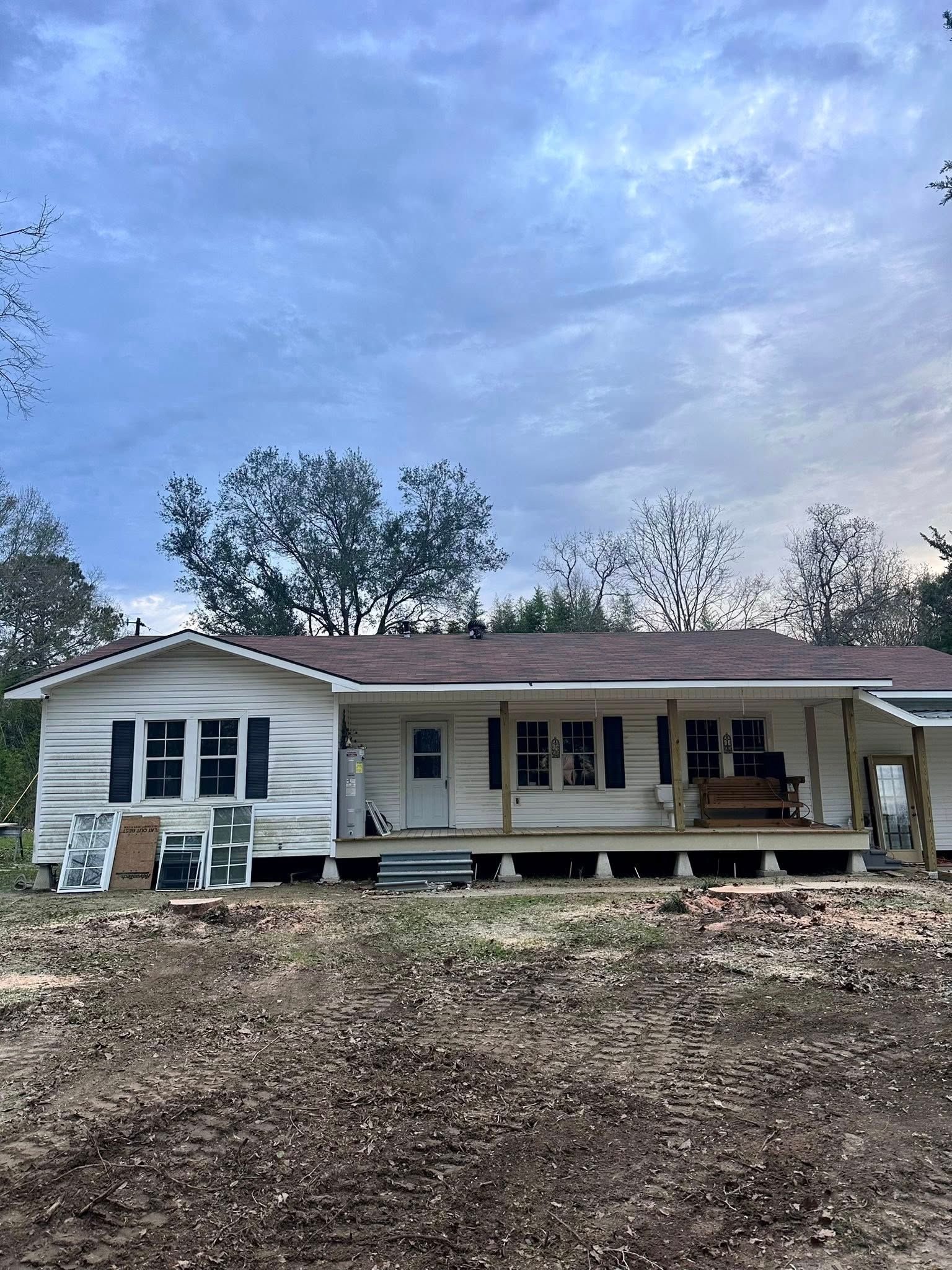 Single-story white house with a front porch on a wooded hillside under a cloudy sky