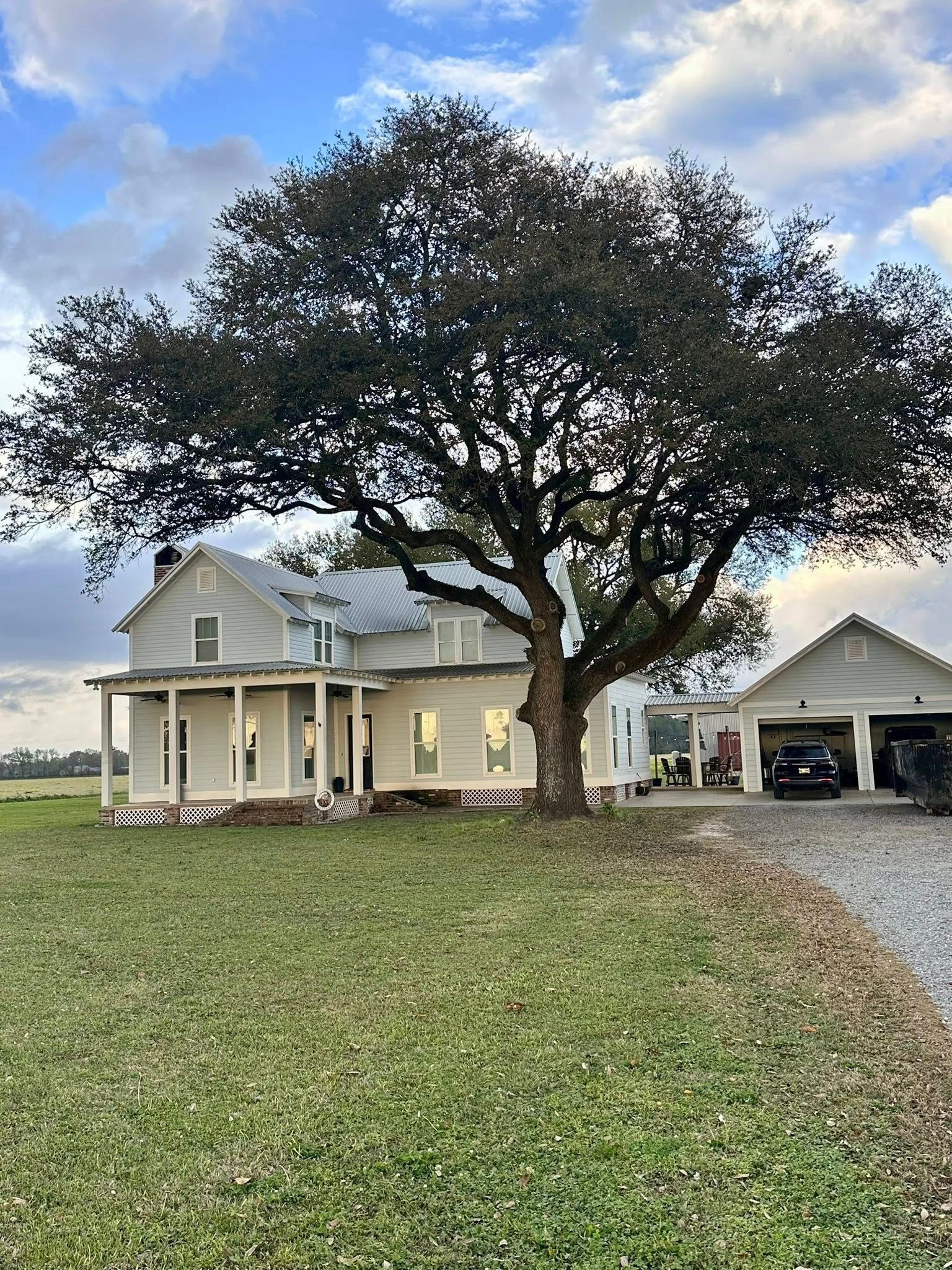 Country house with a large oak tree and detached garage beside a gravel driveway at dusk