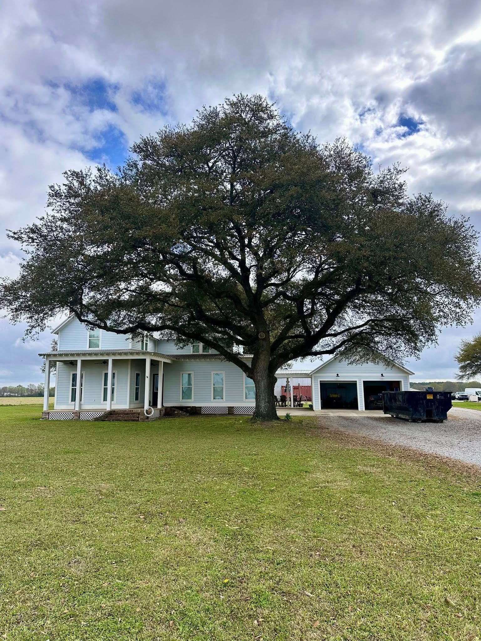 Rural house with a large oak tree in front, cloudy sky, and a truck parked by the carport.