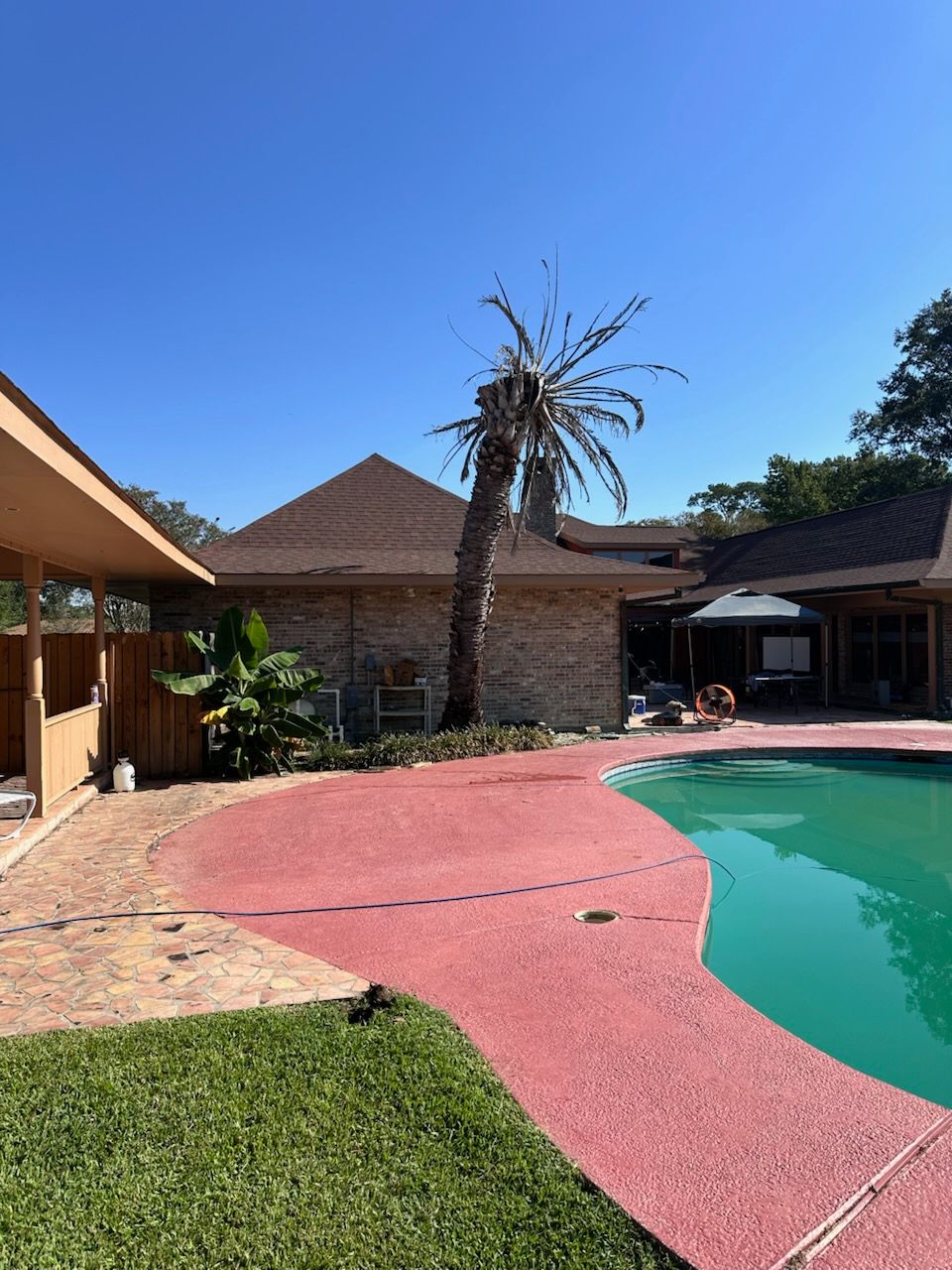 Backyard pool with pink deck, brick house, and clear blue sky