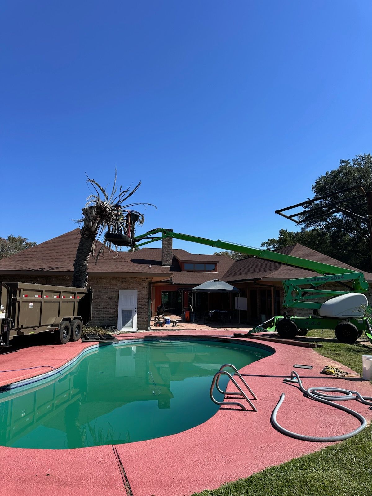 Backyard pool with red deck, house patio, and green pool-cleaning arm under a clear blue sky