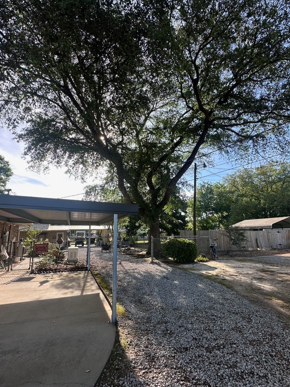 Shady backyard with a large tree, gravel ground, and a covered patio on the left.