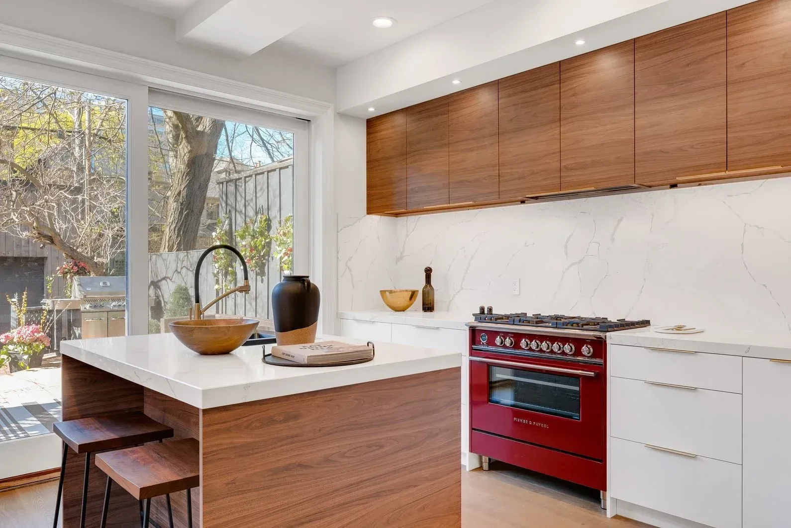 Modern kitchen featuring a wooden island with stools, white countertops, marble backsplash, and a bold red stove.