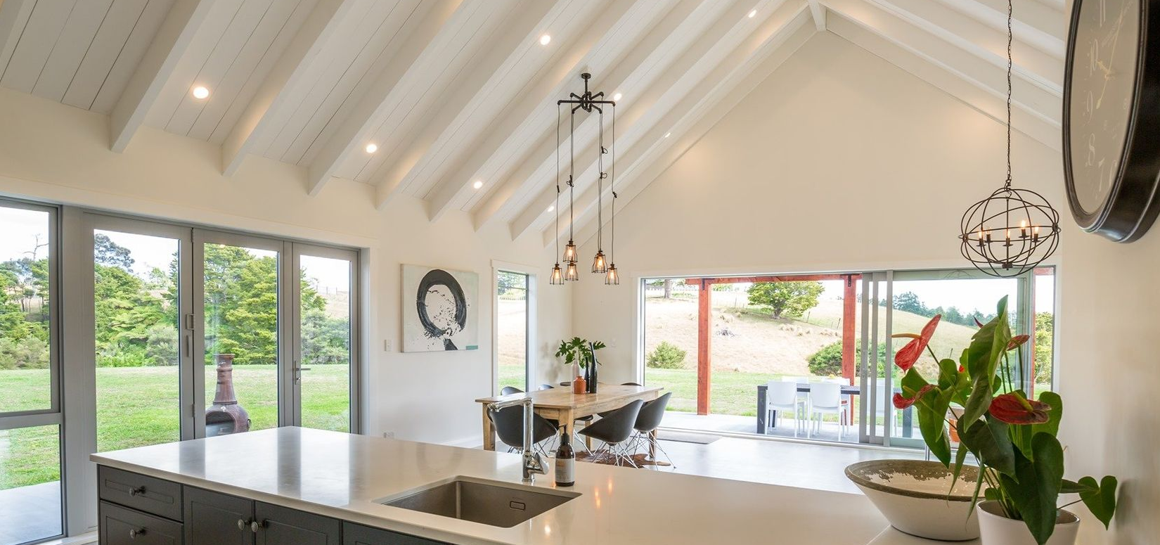Bright, airy kitchen with high vaulted ceilings, white rafters, a central island, and large glass doors opening to a view.