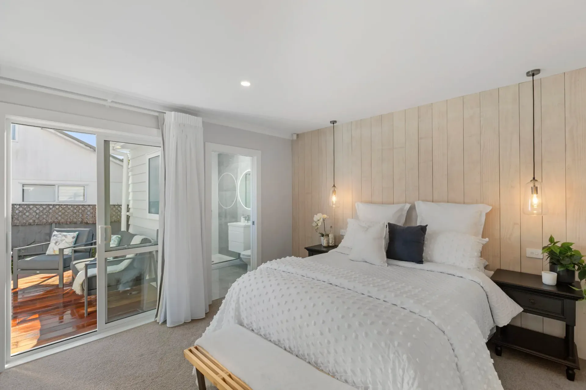 A modern bedroom featuring a bed with white bedding, a light wood paneled wall, two pendant lights, and a sliding glass door.